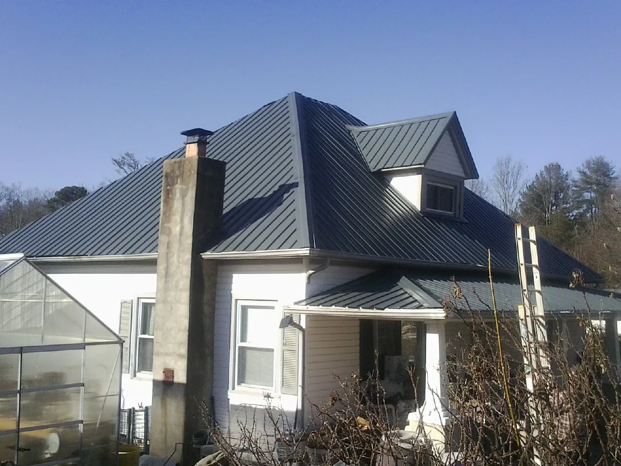 Dark blue standing seam metal roof on a white farmhouse with dormer — Slate & Tile Roof Repair by Roofing Brothers in Fosters