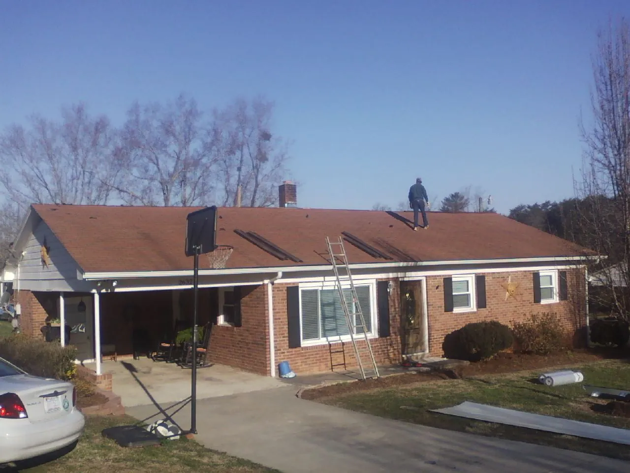 Roofer stripping a shingle roof on a brick ranch before metal panels in Fosters
