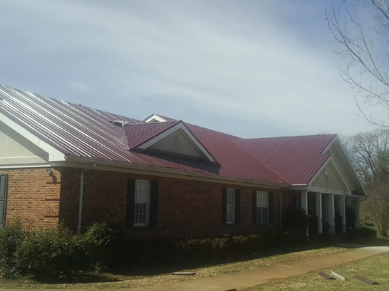 Red metal roof with gabled entries on a long brick building, from a Hail Damage Roof Repair job in Fosters