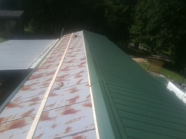 Old rusted panels beside newly installed green metal roofing — Wind Damage Roof Repair by Roofing Brothers in Fosters
