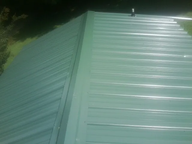 New green metal panels meeting at the ridge of a roof — Flat Roof Repair work by our crew in Fosters