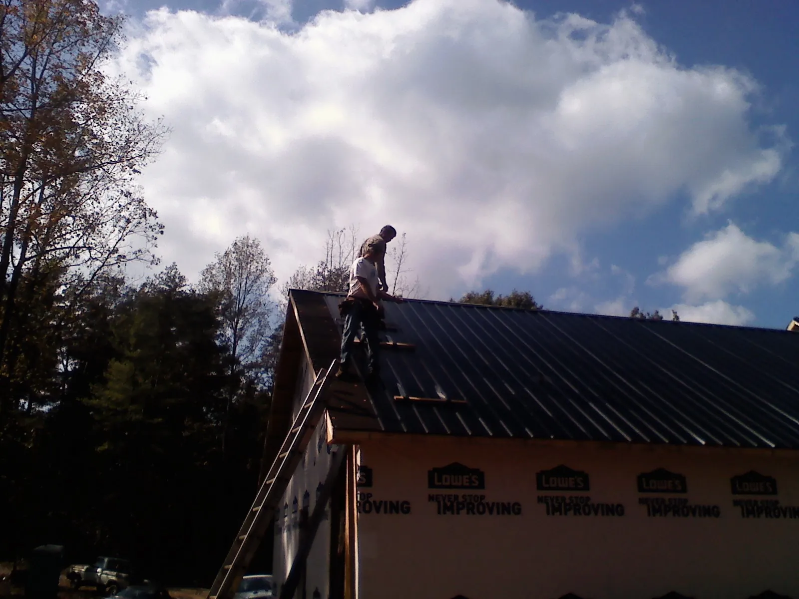Roofer fastening dark metal panels high against a cloudy sky, from a Roof Inspection job in Fosters