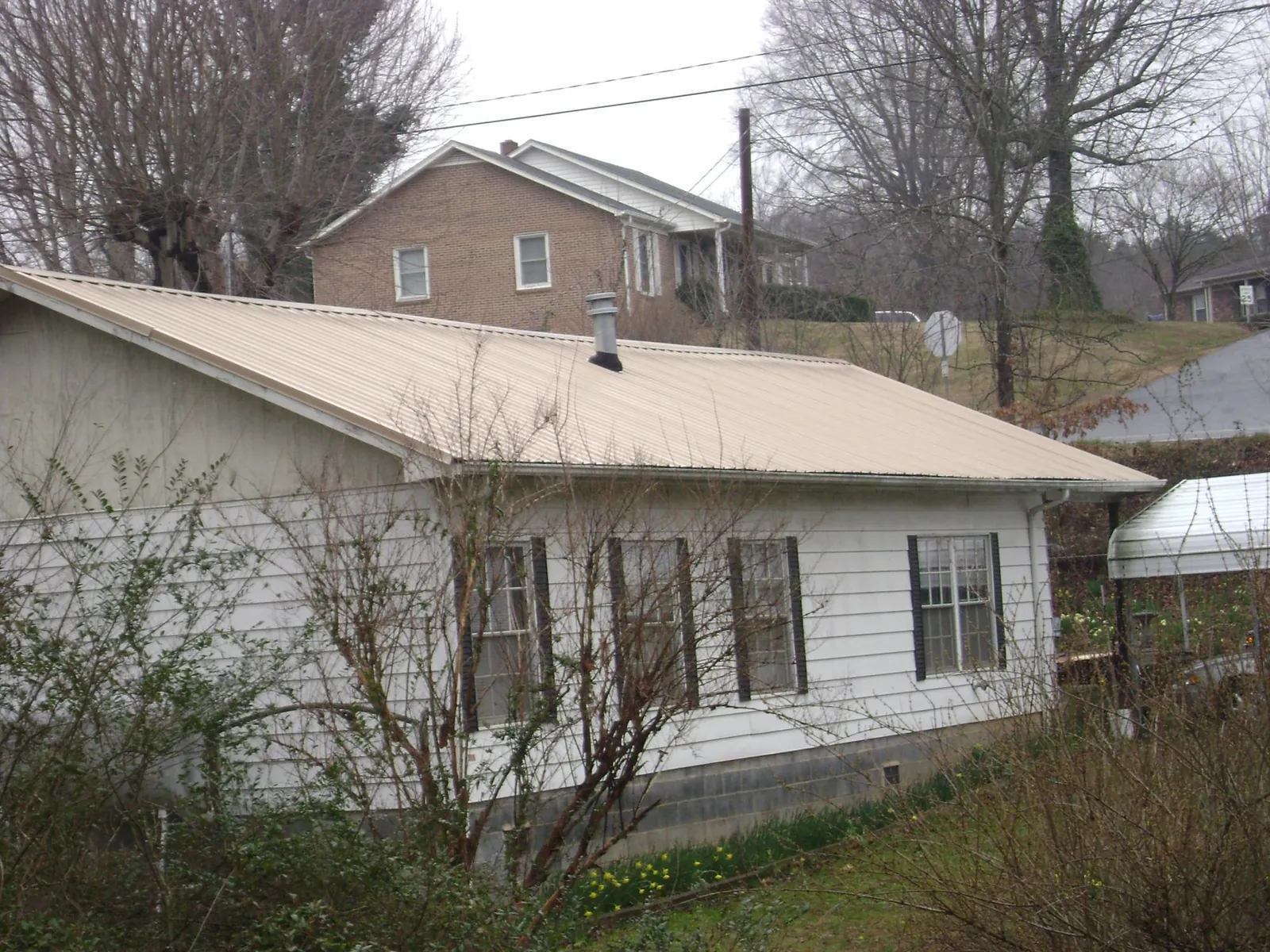 Tan metal roof on a white sided house set into a hillside — Commercial Roofing by Roofing Brothers in Fosters